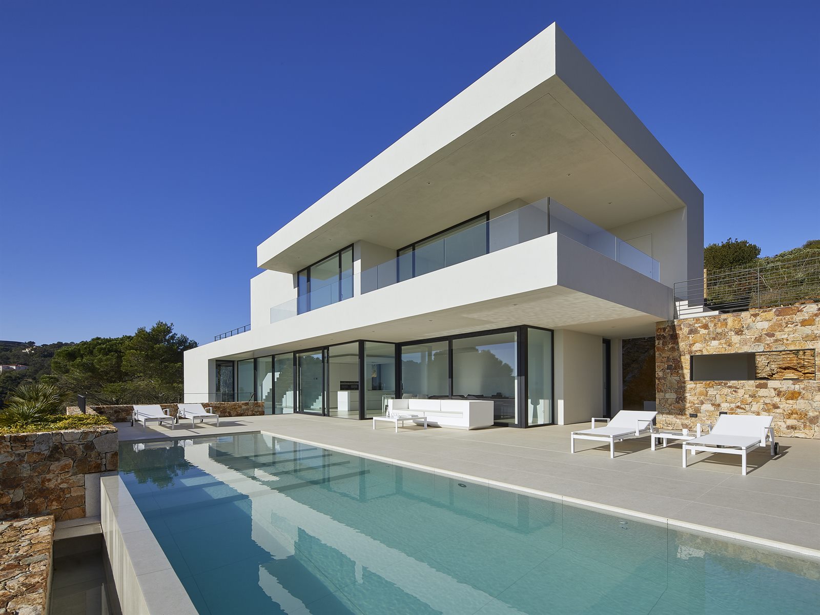 Piscina de hormigón gunitado desbordante integrada en villa contemporánea con muros de piedra en Girona